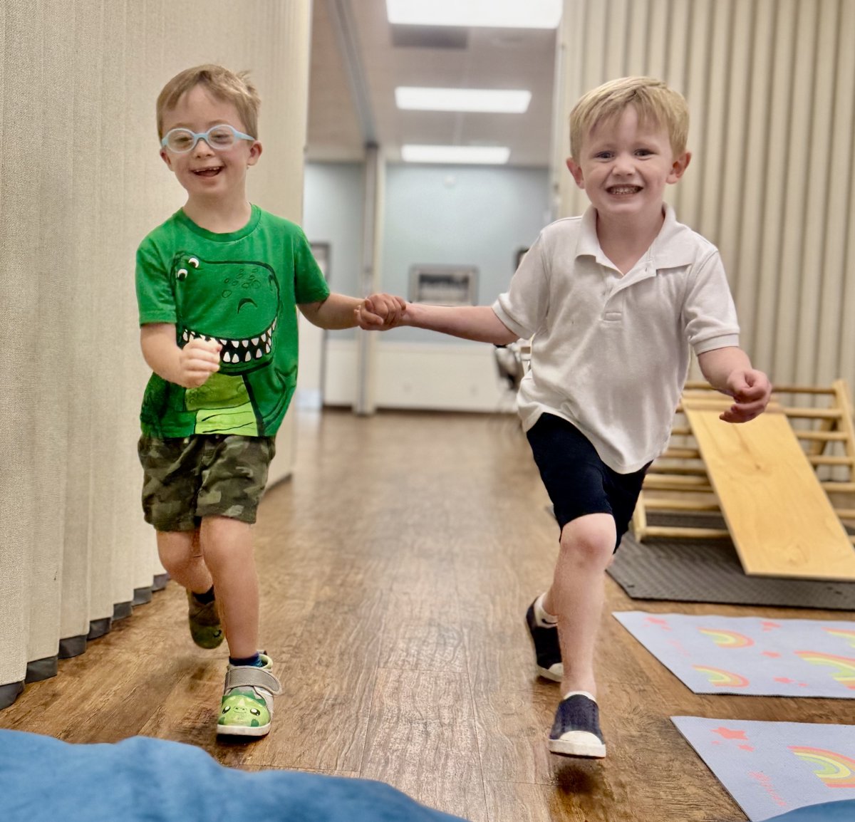 Two young friends running hand in hand down the hallway at Millie's Place Academy