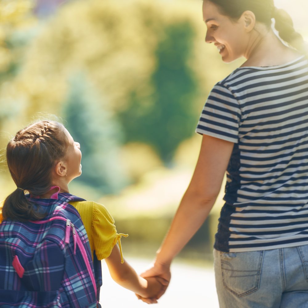 A mother and her young daughter with a backpack walking hand in hand outdoors